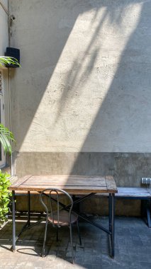 Kaliteli çatı katı tarzı, ahşap sandalyeli ve masalı bir kafeterya. Açık hava oturma alanı, üzerinde güneş ışığı çapraz şekilli beton duvar var.  