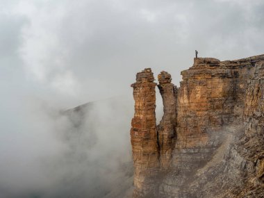 Soft focus. Tourist (man) stands on the cliff edge of Bermamyt plateau on high altitude under cloudy sky in foggy day. Rocks of Big Bermamyt - the so-called 