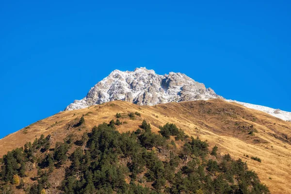 Autumn snow mountains at noon. Bright mountain landscape with a snowy rock in golden sunlight. Natural background of a walk through the rocky mountains with sharp rocks and blue sky.