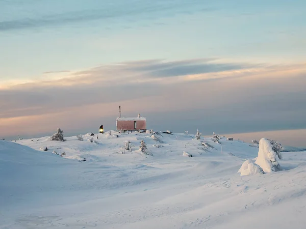 Cozy northern guest house on a snowy hill at dawn. Cabin in winter dawn. Lonely house on a hilltop in the cool morning. Dubldom on the mountain Volodyanaya Kandalaksha, Murmansk region in Russia.