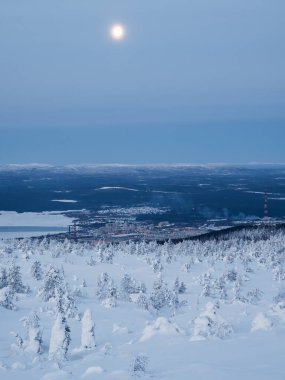 Kuzey Rusya 'nın liman kenti Kandalaksha' nın uzak bir manzarasıyla kışın kutup tepesinin karla kaplı yamacında dolunay. Kış kutup manzarası. Soğuk kış havası. Sert kuzey iklimi