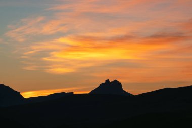 Dark silhouettes of mountains against a bright orange sunset sky. Red sunset over majestic mountains. Sunset in magenta tones. Atmospheric purple landscape with a high-altitude snowy mountain valley. 