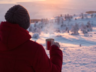 Tea at a frosty sunset. Man with a cup of tea at sunrise. Coffee from the outdoors. Snowy mountain background. Winter holidays, tourism, travel and people concept.