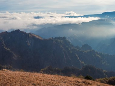 Soft focus. Mountains in a dense fog and sunny slope. Mystical landscape with beautiful sharp rocks in low clouds. Beautiful mountain foggy scenery on abyss edge with sharp forest slopes. Amazing land