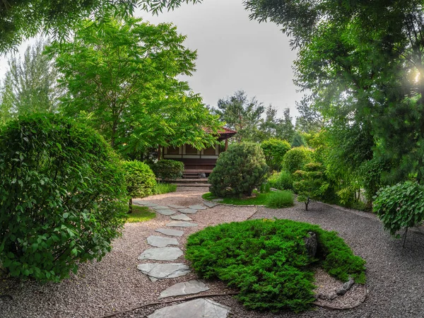Small Japanese garden park style in spring with trees and wooden house on deep garden. The stone pathway to the house.