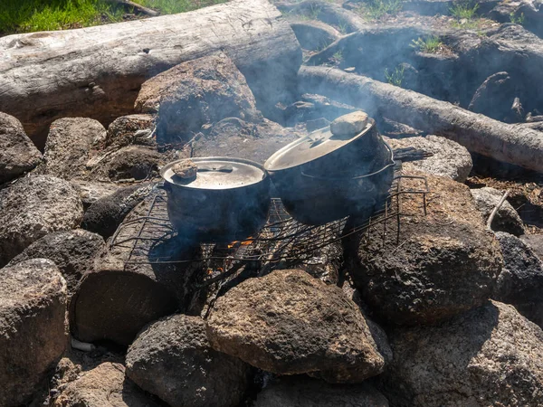 Camping kitchen. Cooking on a campfire in the wild. Two soot-covered kettles stand over the fire. Survival in the wild. Wonderful flame with calderon. Pots in the flames of the fire.