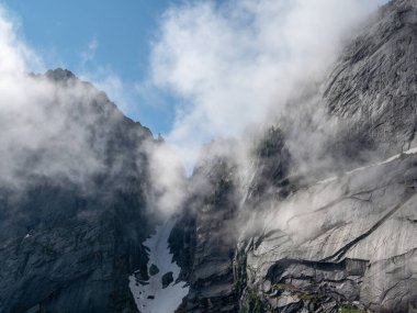 Bulutlarda dağ geçidi. Kasvetli, minimalist, sisli dağ manzarası, karla kaplı. Uçurumun üzerindeki tehlikeli dağ geçidi. Yoğun siste tehlikeli kayalar.