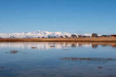 Kosh-Agach Altai Cumhuriyeti 'ndeki manzara. Gölün kıyısındaki köy suyun mavi ayna yüzeyine yansıyor..