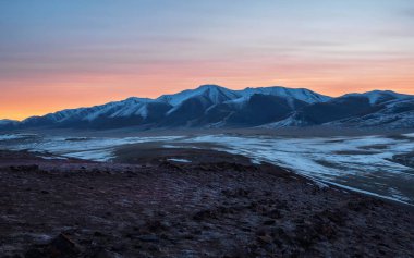 Uzun karlı dağ sıralarıyla panoramik dağ manzarası alçak bulutlar arasında şafak güneşi tarafından aydınlatılıyor. Gün batımında ya da gündoğumunda yüksek dağ sırtı olan harika bir dağ manzarası. Üzerinde turuncu ışık olan buzullar..