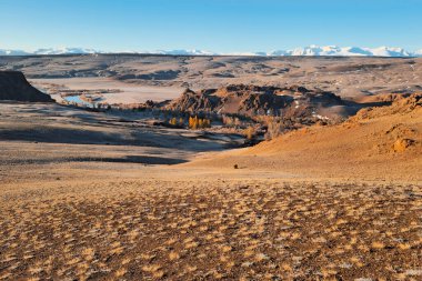 Parlak sonbahar dağ bozkırları. Güneş ışığında geçitten dağ vadisine harika bir dağ manzarası ve ufukta harika dağ siluetleri. Altai bölgesi.