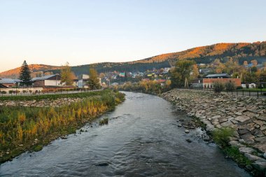 Bir dağ nehrinin kıyısındaki akşam köyü. Kırsal alan. Nehrin kayalık yatağı köyün içinden akıyor. Gorno-Altaisk. Mayma Nehri.