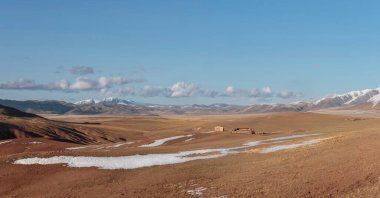 Parlak sonbahar dağ bozkırlarının geniş panoramik manzarası. Güneş ışığında geçitten dağ vadisine müthiş bir dağ manzarası ve ufukta mavi gökyüzünde beyaz bulutlar olan büyük dağ siluetleri..