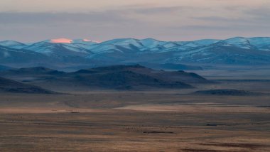 Gün batımında yumuşak dağlar. Görkemli dağların üzerinde mor gün batımı. Mor tonlarda gün batımı. Yüksek rakımlı karlı dağ vadisi olan atmosferik mor bir manzara. Altai bölgesi, panoramik görünüm.