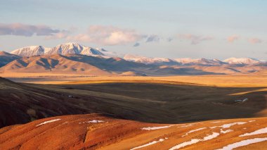 Günbatımında sonbahar kar dağları. Parlak panoramik dağ manzarası ve altın güneş ışığı altında karlı bir kaya. Keskin kayalar ve mavi gökyüzü ile kayalık dağlarda yürümenin doğal arka planı.