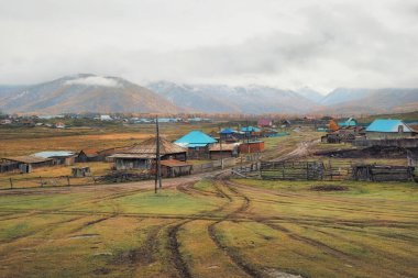 Bir tepeden uzak bir köye sonbahar toprak yolu. Sonbahar karaçamalı uzak bir ormanlık alanda, yamaçta ıslak, virajlı toprak bir yol. Altai bölgesindeki köye giden dağ sonbaharı off-road pisti.