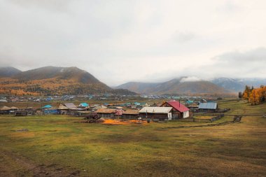Altai dağlarındaki bir köyün önündeki sonbahar tarlası. Dağın altında küçük bir köy. Rusya 'nın Belyashi köyünde karlı ve sisli bir sabahın altın sonbahar manzarası
