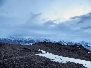 Sabahın erken saatlerinde dağın tepesinde dağcı figürleri. Alçak bulutlarda karla kaplı dağın puslu minimalizmi. Moğolistan 'da turizm.