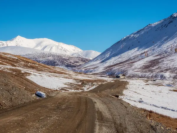 Long and winding road to distance. Picturesque autumn landscape with a rocky dirt road through the stone  steppe in the mountains with the first snow on top mountains.