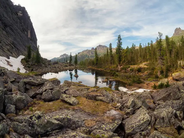 Mountain forest lake among large rocks. Alpine lake among stone meadows in high mountains. Taiga summer landscape. Perfect panoramic image for wall, screen. Scenic artwork.