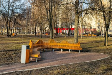 Şehir parkındaki ortopedik ahşap banklar. İlkbaharda gökdelenlerin arka planında şehir parkında yuvarlak bank. St. Petersburg, Rusya 'daki cadde ve parkların düzenlenmesi.