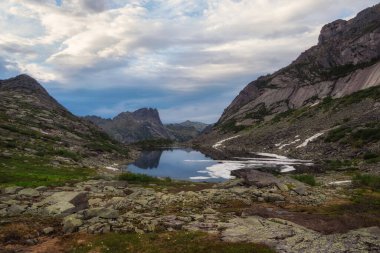 Bir dağ gölünde alacakaranlık. Alacakaranlıkta kayaların arasında küçük güzel bir göl. Alp gölü ve kayalık yüksek dağlarla manzaralı bir yer. Batı Sayans 'taki Dağ Gölü.
