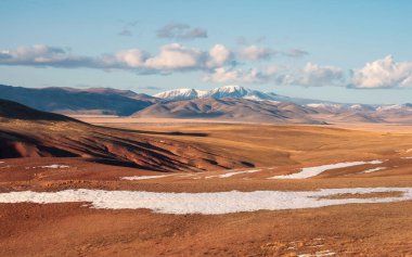 Kuzey Chui tepesinin geniş panoramik dağ manzarası, karlı dağ zirveleri ve altın sonbahar bozkırları. Duvar, ekran ve sanat eserleri için mükemmel sonbahar resmi.