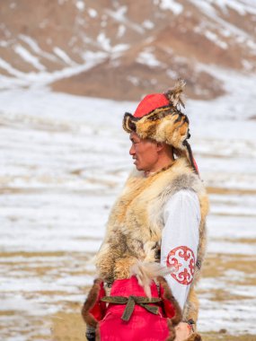 Ulgii, Moğolistan - 01 Ekim 2023: Moğolistan bozkırında bir Moğol erkek avcının portresi. Kuzey Moğolistan. Geleneksel giysiler içinde genç bir Moğol bir kayanın önünde duruyor. Yukarıdan görüntüle.