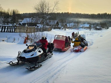 Perm Region, Rusya - Ocak 05, 2024: İnsanlar kışın kayak yapmak için şişme bir muza otururlar. Eğlence gezileri, halk kış eğlenceleri. Kar arabası turistlerle dolu şişme bir muz çekiyor..