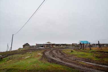 Toprak yolu olan kırsal bir manzara. Dağın altında küçük bir köy. Elektrik hattı kabloları ve direkler. Rusya 'nın Belyashi köyünde kasvetli bir sonbahar sabahı manzarası, Altai Krai.