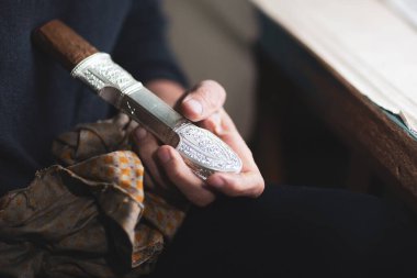 Seçici odaklanma. Kubachin kuyumcusunun elleri yakın planda gümüş bir hançer sapı tutuyor. Bireysel mühendislik üretim kavramı.