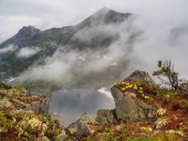 Hayalet dağ gölü. Huzurlu meditasyon havası, aşağıdaki bir dağ vadisinde bulunan buzul gölü manzarası sisli sabahın erken saatlerinde sivri tepelerle çevrili..