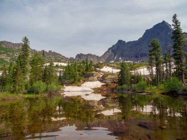 Tırtıklı tepeleri olan yüksek dağlar. Dağ vadisi, Sibirya 'nın kayıp dünyası. Aynadan yansıyan temiz göl dağların arasında gizlidir, yaz doğasında orman vardır..