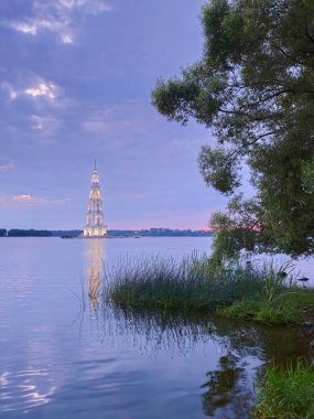 Adadaki çan kulesinin üzerinde göz kamaştırıcı bir mavi saat, minimum gün batımı manzarası. Kalyazin, Rusya 'da Volga nehrindeki ortodoks kilisesini sular altında bıraktı. Göldeki çan kulesi. Volga nehri boyunca dolaşın.. 