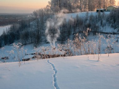 Kardan geçerek karla kaplı bir vadideki kulübeye giden ayak izleri. Duman bacadan dışarı çıkıyor. Rus kırsalında, gerçek hayatta. Cherdyn..