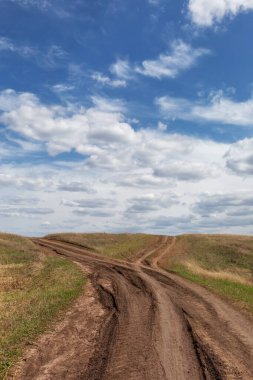 Toprak yolda yol ayrımı, yol seçimi. Büyük dağlarda uzun bir yol. Dikey görünüm. Arazide asfalt olmayan eski bir yol, mavi gökyüzü olan yaz manzarası.