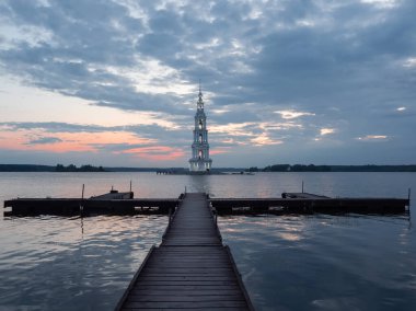 Uzun ahşap iskele. Adadaki çan kulesinin üzerinde çarpıcı bir alacakaranlık, minimalist günbatımı manzarası. Kalyazin, Rusya 'da Volga nehrindeki ortodoks kilisesini sular altında bıraktı. Göldeki çan kulesi.. 