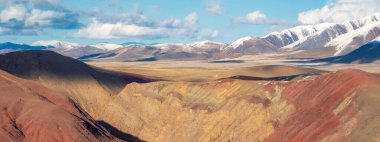 Kuzey Chui tepesinin geniş panoramik manzarası, karla kaplı dağ zirveleri ve altın sonbahar Kurai bozkırları. Sarı bozkır ve gün batımında karanlık dağlar.