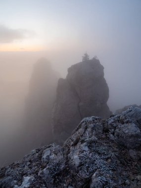 Fog in the canyon with big rock in sunrise. Atmospheric ghostly landscape with fuzzy silhouettes of sharp rocks in low clouds. Dramatic view to large mountains blurred in rain haze in gray low clouds. clipart