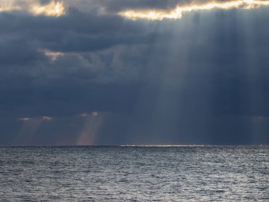 Karadeniz üzerinde gün batımında kara bulutlar. Gökyüzü ve bulutların alacakaranlık mavisi renginde dramatik bir günbatımı. Güneş ışınları ve denizde gökyüzünde bulutlar. Doğa soyut bir bileşimdir.. 