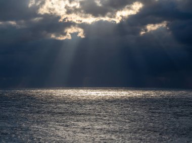 Karadeniz üzerinde gün batımında kara bulutlar. Gökyüzü ve bulutların alacakaranlık mavisi renginde dramatik bir günbatımı. Güneş ışınları ve denizde gökyüzünde bulutlar. Doğa soyut bir bileşimdir.. 