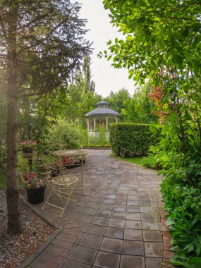 Yaz bahçesi avlusu. Yaz parkının güzel peyzajı. Bahçenin dibinde açık bir çardak var. Açık Bahçe Dekorasyonu. Abakan. Dikey görünüm. 