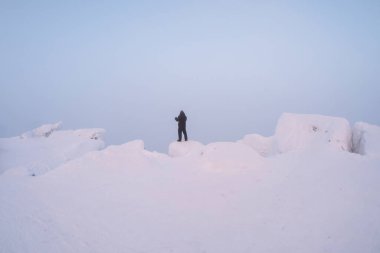 Yumuşak odaklanma. Adam pembe gün batımında karlı beyaz bir dağın tepesinde duruyor. Sert kış. Soğuk doğal arkaplan.
