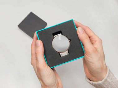 Zarif paketlerin içinde bulunan son elektronik saati aktif olarak açan bir kadının yakın görüntüsü. Koruyucu filmli bir kutuda yeni bir akıllı saat. Üst görünüm.