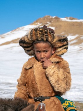 Ulgii, Moğolistan - 30 Eylül 2023: geleneksel kış kürklü giysileri giyen kafası karışmış bir Moğol çocuğunun portresi. Moğol bozkırının ortasında güneşli bir gün.