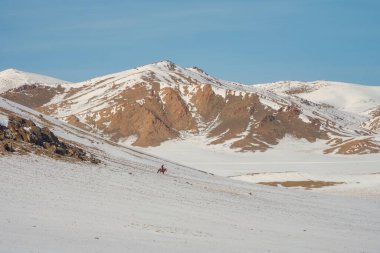 Siluet süvari at sırtında kar yamacının tepesinde berrak mavi bir gökyüzüne karşı. Güzel Moğol manzaralı kar dağı. Atlı küçük bir binici figürü..