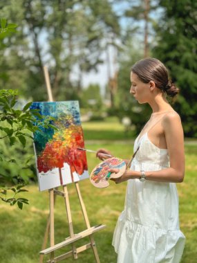 Genç, güzel bir sanatçı bir yaz parkında yalın bir havada resim yapıyor..