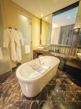 Abu Dabi, BAE - 30 Mayıs 2024 Grand Hyatt Abu Dabi Oteli 'ndeki karanlık banyo. Ön planda bir küvet. Dikey görünüm.