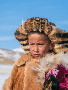 Ulgii, Moğolistan - 30 Eylül 2023: geleneksel kış kürklü giysileri giyen kafası karışmış bir Moğol çocuğunun portresi. Moğol bozkırının ortasında güneşli bir gün.