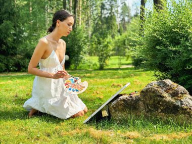 Bahçesinde ince bir kız resmi var. Genç, güzel bir sanatçı bir yaz parkında yalın bir havada resim yapıyor..