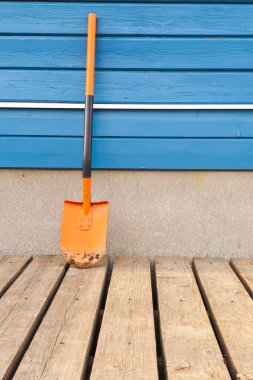 Kirli bahçe turuncu küreği gölgeli ahşap duvarın yanında. Dikey görünüm. Boşluğu kopyala. 